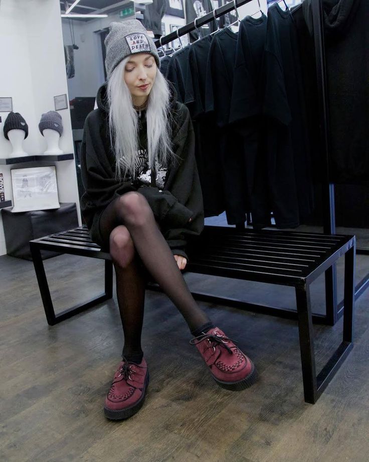 a woman with long white hair sitting on a bench in a clothing store wearing red shoes