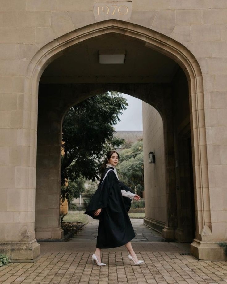 a woman in a graduation gown is walking through an archway