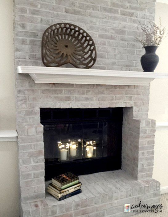 a white brick fireplace with candles on top and some books in the corner next to it