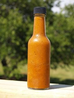 a bottle filled with orange sauce sitting on top of a wooden table next to trees