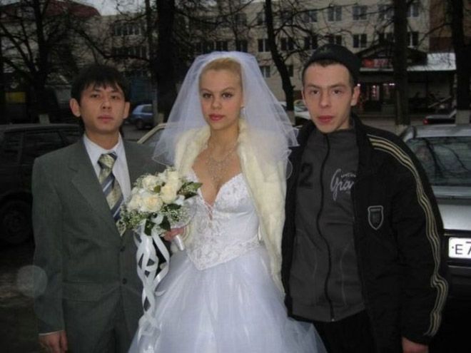 two men and a woman standing next to each other in front of a car on the street