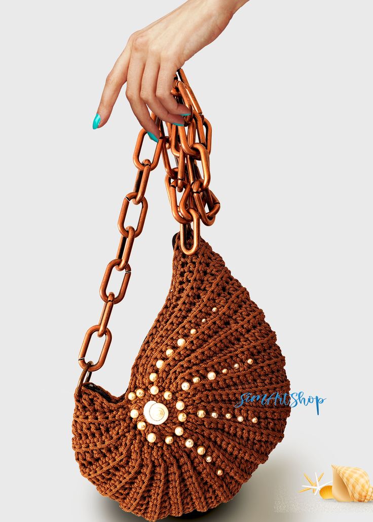 a woman's hand holding a brown crocheted purse with chains on it