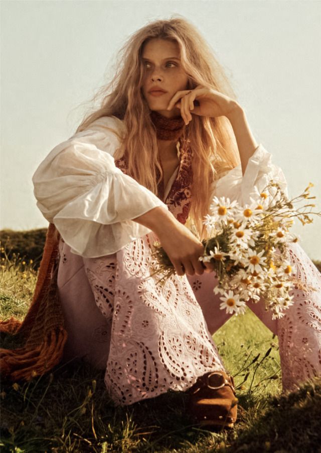 a woman sitting on the grass with flowers in her hand and looking at the camera