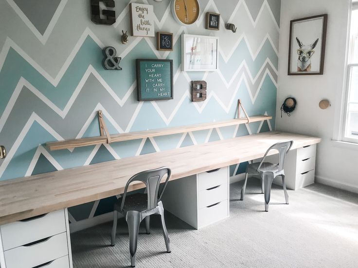 a desk with two chairs in front of a wall decorated with chevroned blue and white paint