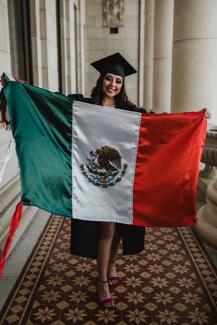 a woman in graduation cap and gown holding a mexican flag on a carpeted floor