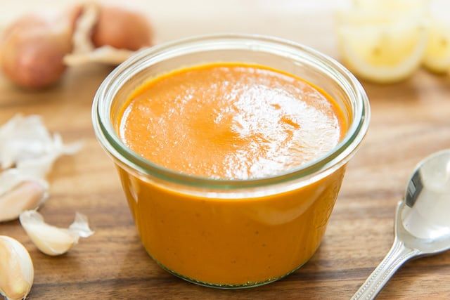 a glass jar filled with sauce sitting on top of a wooden table next to garlic