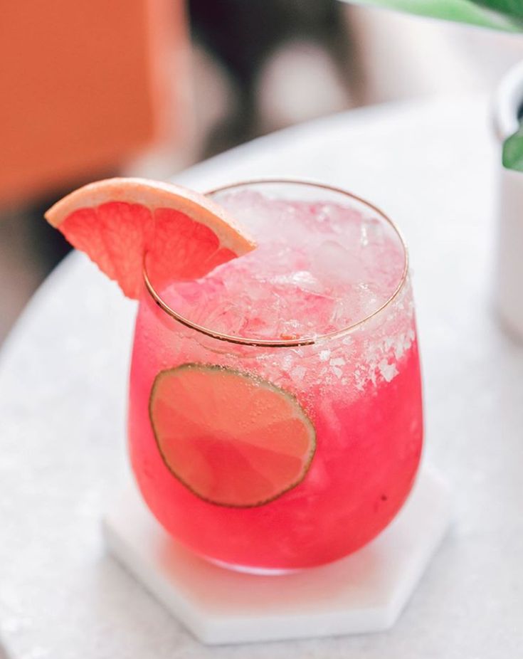 a pink drink with a slice of watermelon on the rim and garnish