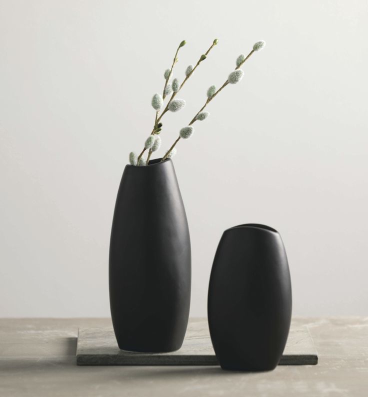 two black vases sitting on top of a table next to each other with flowers in them