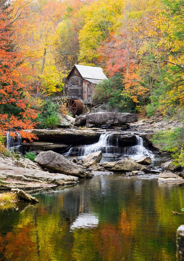 an old mill sits on the edge of a river surrounded by fall foliage and trees