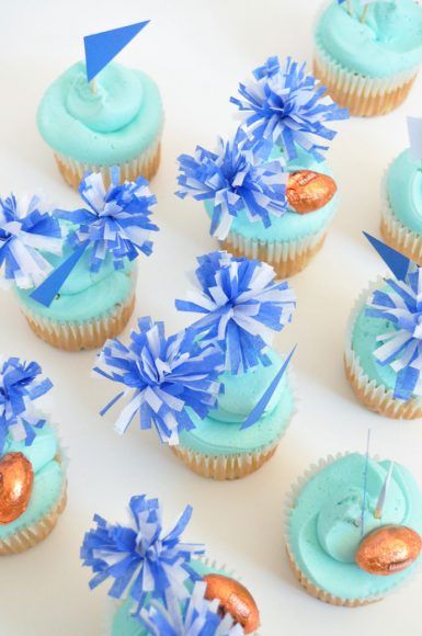 cupcakes with blue frosting and decorations on white table top next to each other