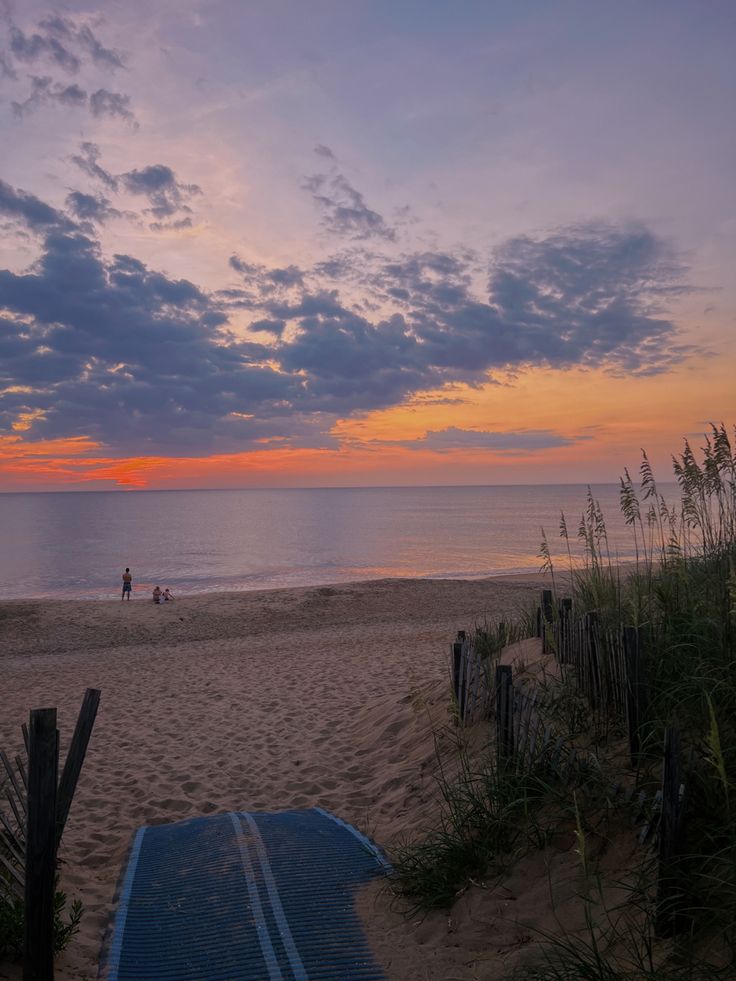 the sun is setting at the beach and people are walking on the sand near the water