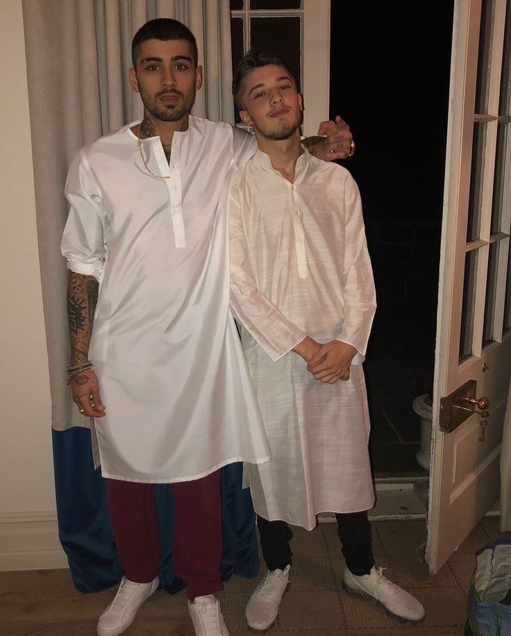 two men standing next to each other in front of a door wearing white shirts and red pants