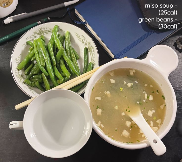 a bowl of green beans and soup with chopsticks next to it on a table