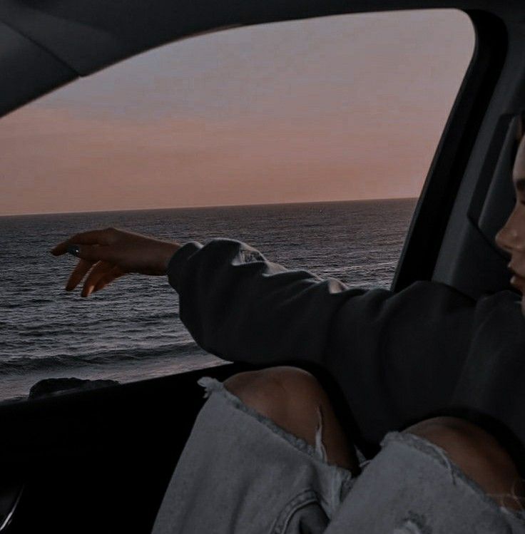 a woman sitting in the passenger seat of a car looking out over the ocean at sunset