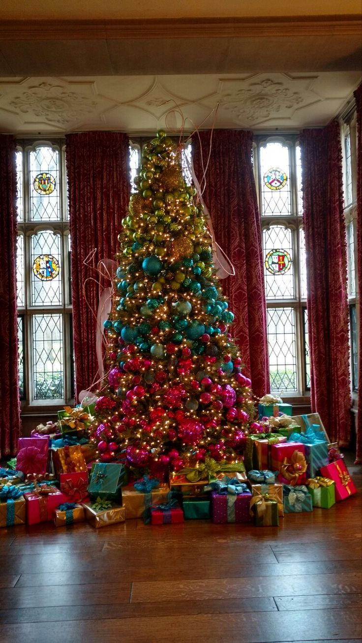 a christmas tree is surrounded by presents in front of two windows