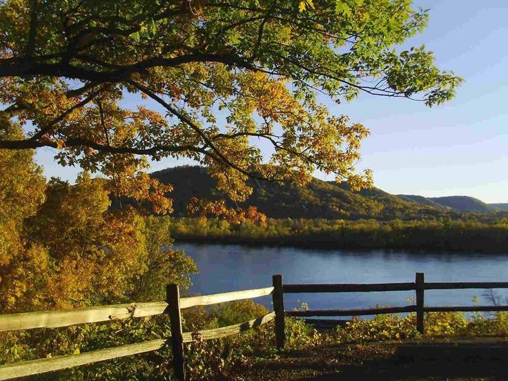 a wooden fence sitting next to a lake surrounded by trees with fall foliage on it