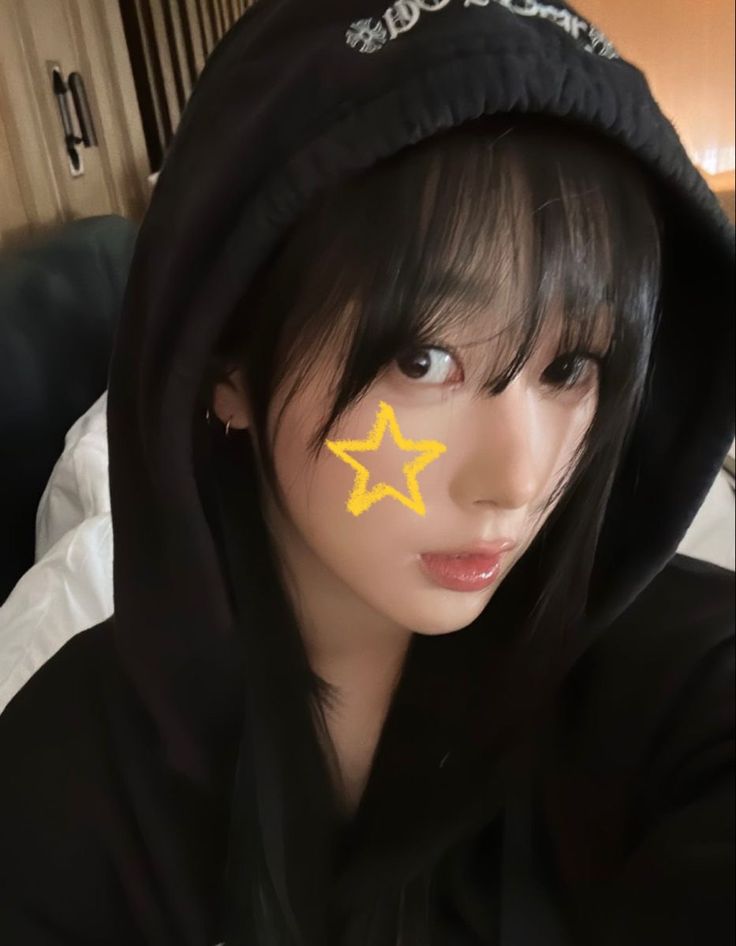 a girl with a yellow star painted on her face and hoodie over her head