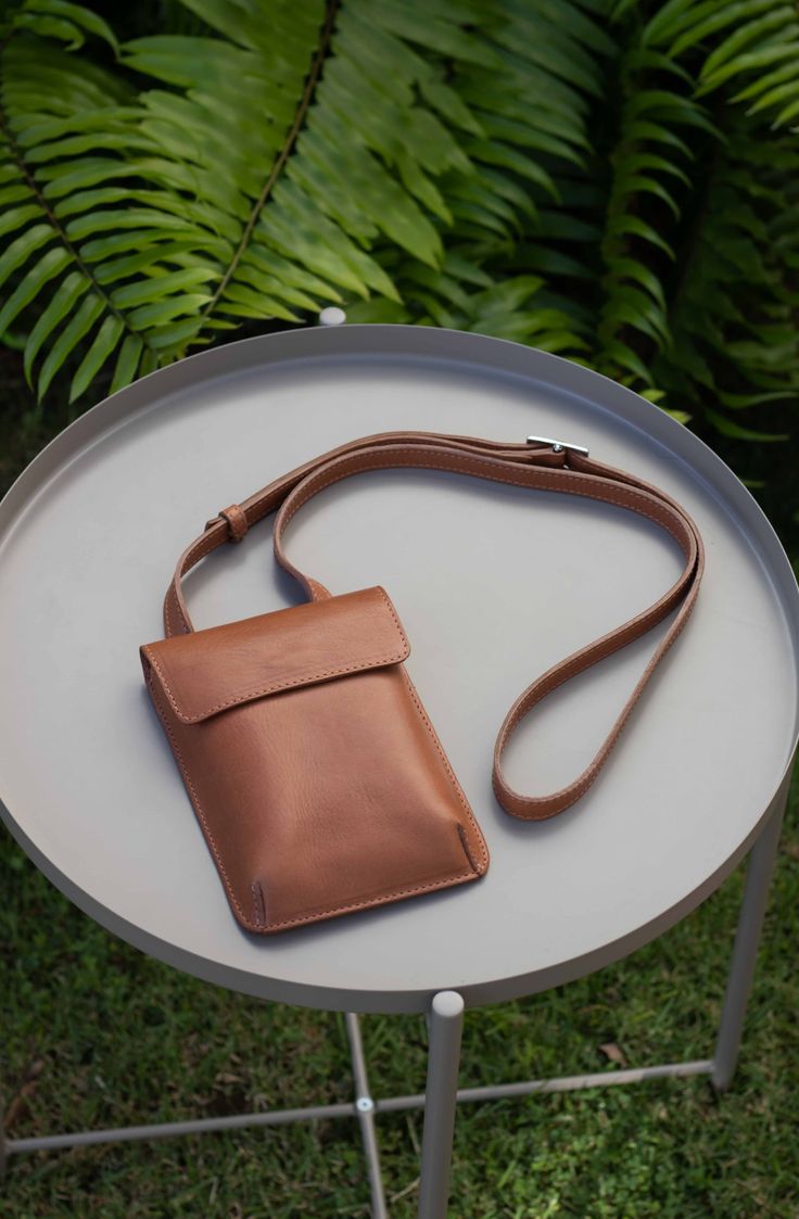 Vegetable tanned leather shoulder pouch. Funcional and compact design. The mini shoulder bag is a convenient way to carry around your essentials. It has enough space for a phone of any size, pen, passport, cards, keys and more. Front flap closure with magnetic snap. Inner money-card pocket and adjustable strap with buckle. Beige cotton lining.Handcrafted in Argentina by artisans in small batches, with every detail taken care of. Dust bag included for proper storage. Dimensions: - Height: 7”- Wid Classic Phone Bag Pouch For On-the-go, Classic Phone Bag With Removable Pouch As Shoulder Bag, Classic Pouch Shoulder Bag With Mobile Phone Holder, Classic Shoulder Bag With Mobile Phone Pouch, Travel Shoulder Bag With Cell Phone Pocket And Flap, Versatile Shoulder Bag With Snap Closure For On-the-go, Classic Phone Bag With Removable Pouch For Everyday, Leather Phone Shoulder Bag For Everyday Use, Leather Shoulder Phone Bag For Everyday Use