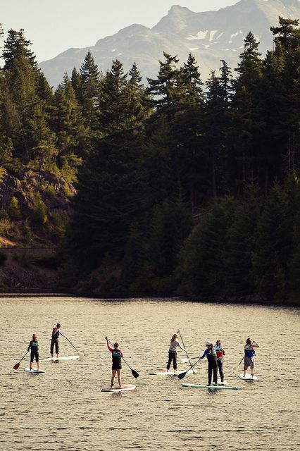 there are many people on paddle boards in the water with trees and mountains behind them