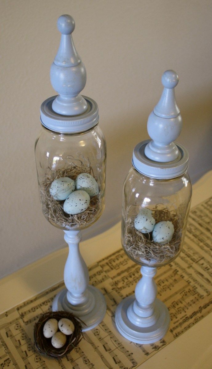 two glass jars with eggs in them sitting on a table next to a bird's nest