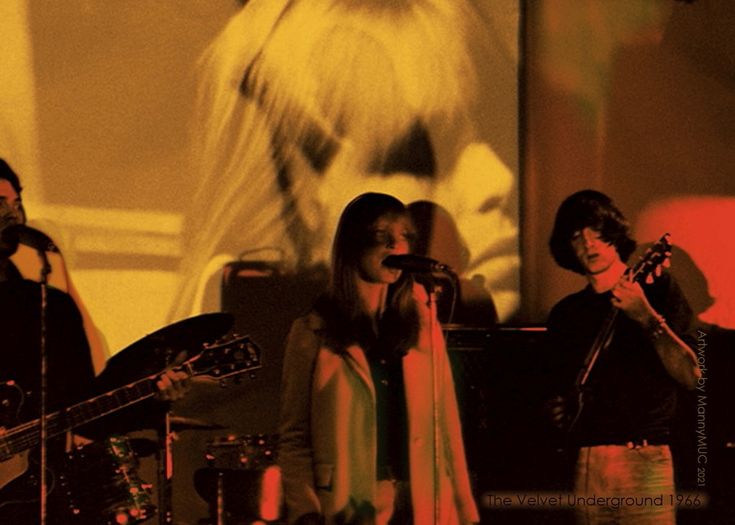 three people on stage singing and playing instruments in front of a woman with long hair