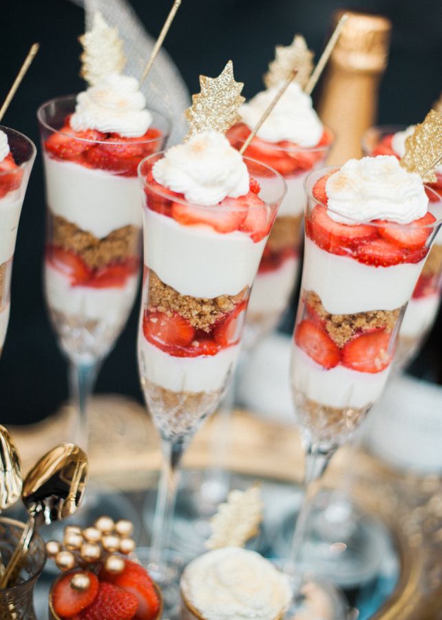 desserts are arranged in small glasses with strawberries and whipped cream on the rim