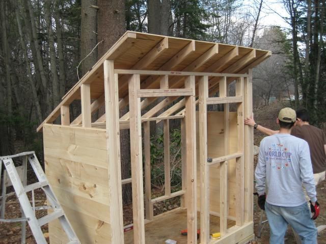 two men are building a small house in the woods with wood framing on the walls