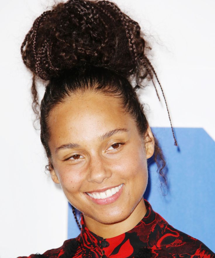 a woman with curly hair wearing a red and black shirt smiles at the camera while standing in front of a blue wall