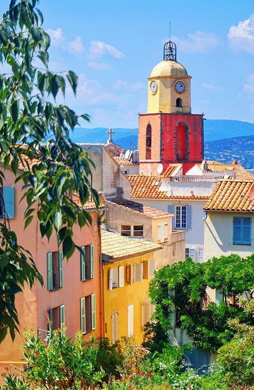 a clock tower in the middle of some buildings with trees and mountains in the background