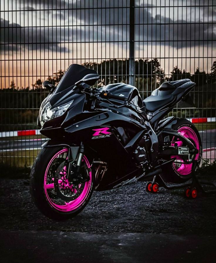 a black and pink motorcycle parked in front of a fence at night with the sun setting