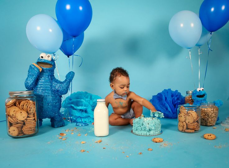 a baby is sitting in front of some cookies and cake with blue balloons on it