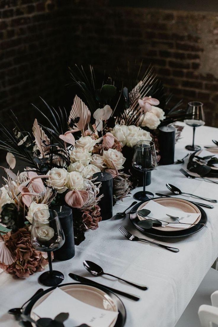 the table is set with black and white plates, silverware, and floral centerpieces