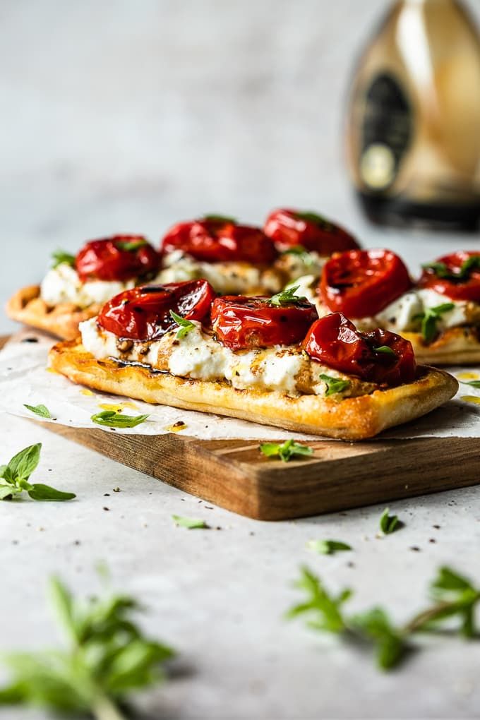 two pizzas with tomatoes and cheese on a cutting board