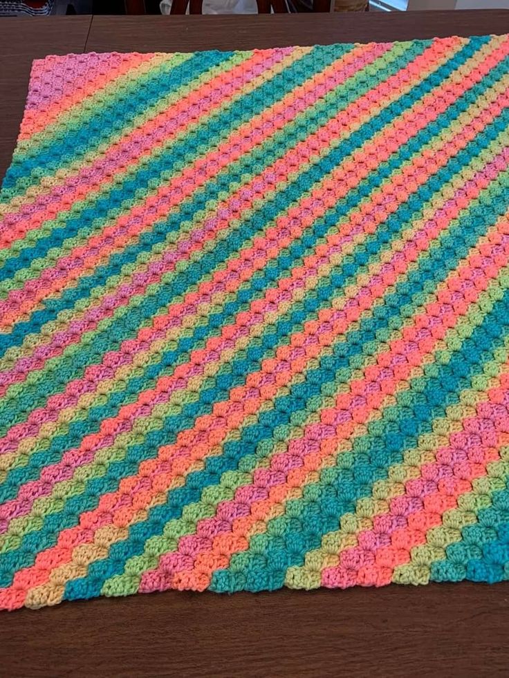 a multicolored crocheted blanket sitting on top of a wooden table