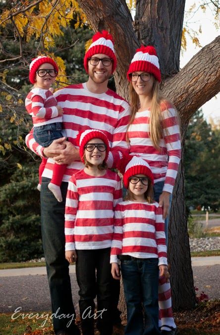 a family wearing matching red and white striped outfits in front of a tree with fall leaves