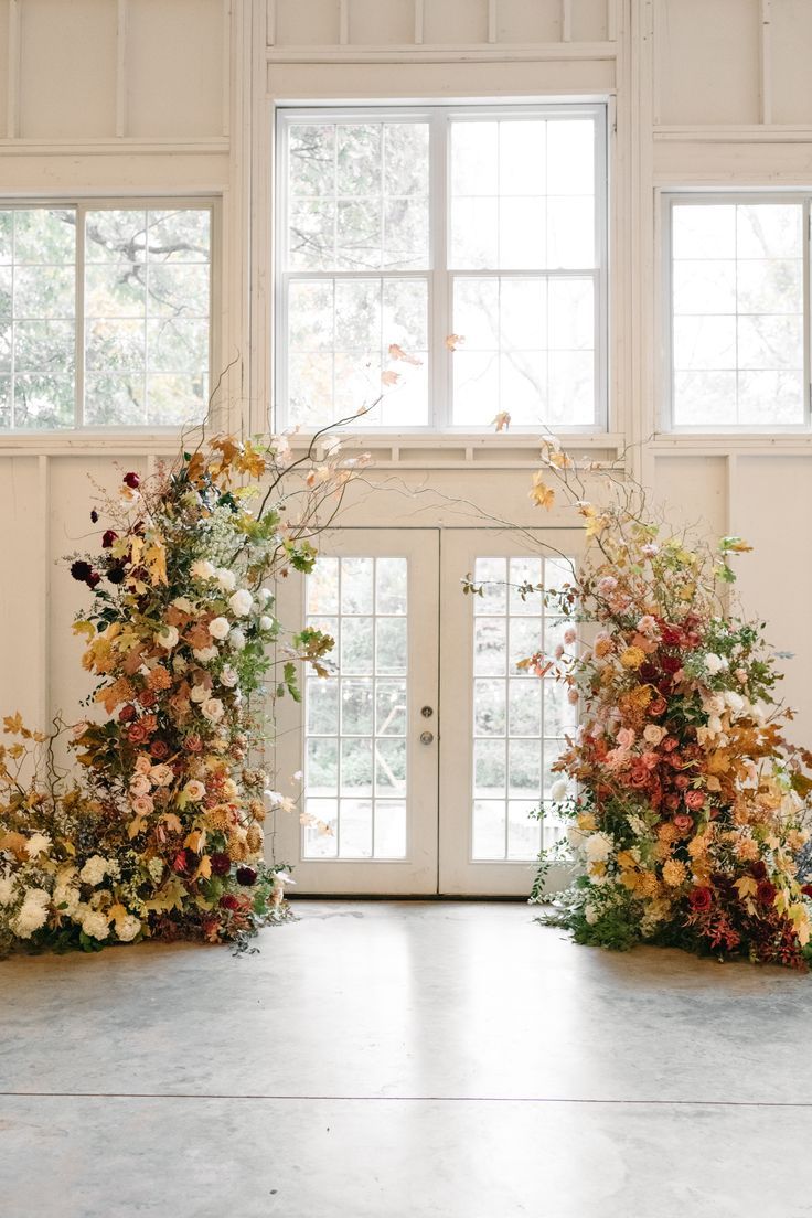 an entrance decorated with flowers and greenery in front of two large white doors that lead into the room