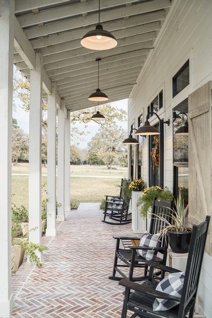 black rocking chairs on the front porch of a white house with brick flooring and large windows