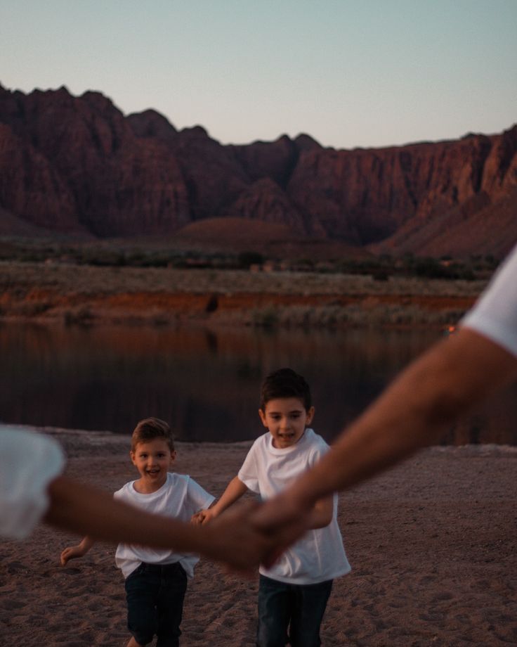 two young children holding hands in front of a mountain range at sunset with mountains in the background