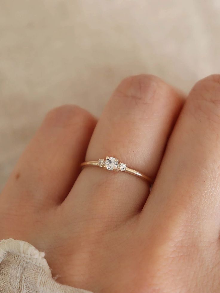 a woman's hand wearing a gold ring with three diamonds on it and the middle finger