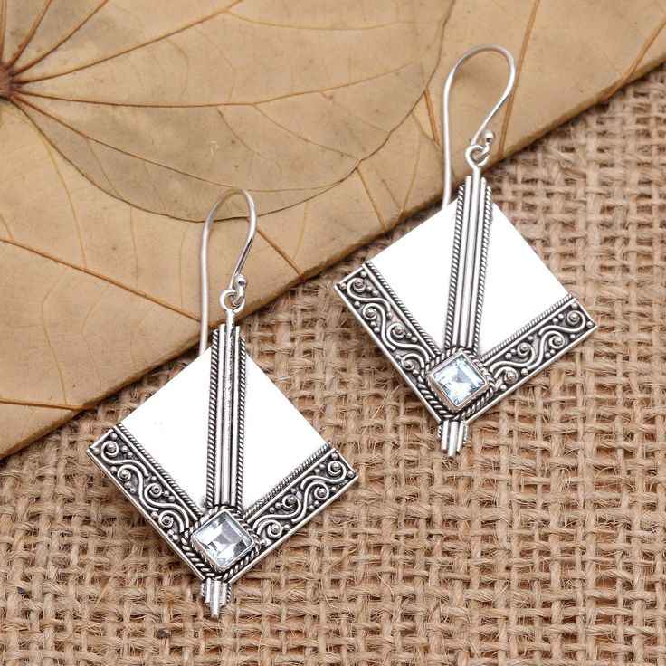 With their diamond-shaped panels of gleaming silver Made Mustika's dangle earrings are truly unique. The Balinese artisan bisects the panel with three sterling silver rods which lead to a square blue topaz stone in a bezel setting. A decorative engraving borders the bottom edges of the earrings while sterling silver hooks finish the exquisite pair. Nickel Free Silver Diamond-shaped Jewelry, White Sterling Silver Art Deco Jewelry, Art Deco Silver Jewelry With Diamond Accents, Silver Diamond-shaped Earrings For Anniversary, Rectangular Sterling Silver Earrings With Diamond Accents, Sterling Silver Rectangular Earrings With Diamond Accents, Silver Diamond-shaped Earrings With Diamond Accents, Silver Topaz Jewelry With Rectangular Stone, Silver Diamond-shaped Earrings For Gift