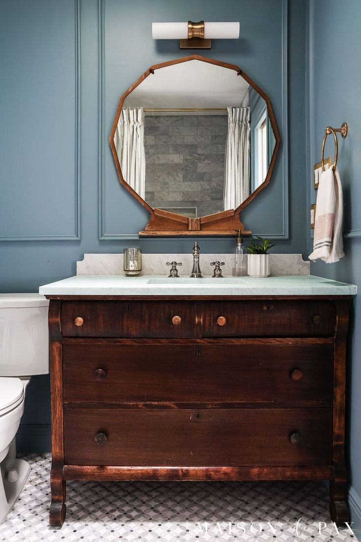 a bathroom with blue walls and a wooden dresser under a mirror in front of a white toilet