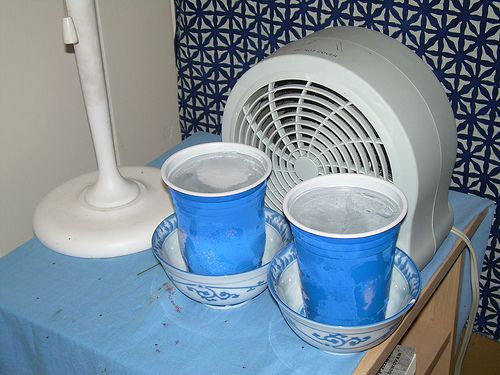 three blue cups sitting on top of a table next to an air conditioner and fan