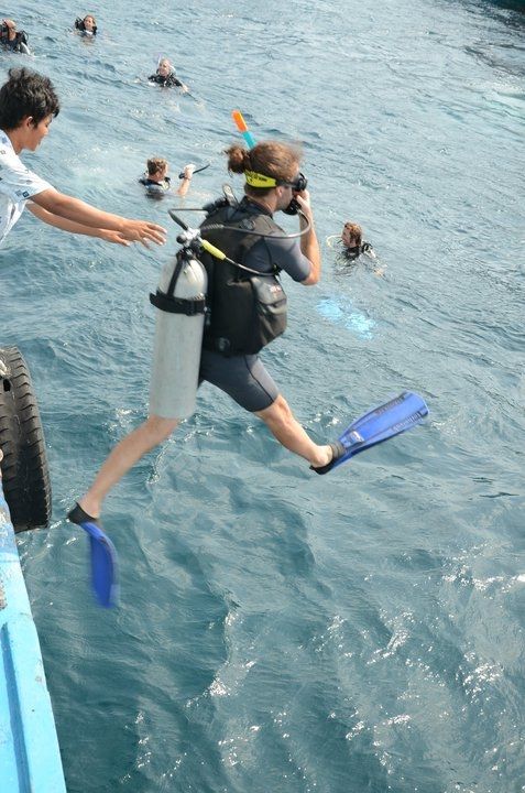 a man jumping into the water from a boat with people swimming behind him and holding onto their feet