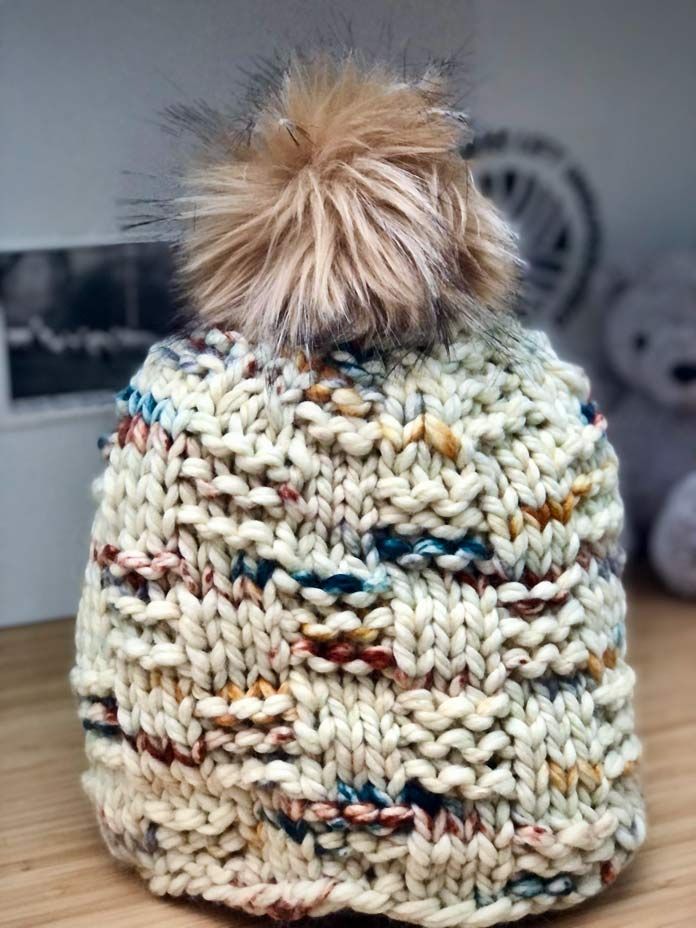 a knitted hat with a pom - pom sits on a wooden table