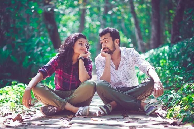 a man and woman sitting on the ground in front of trees, one is holding her mouth