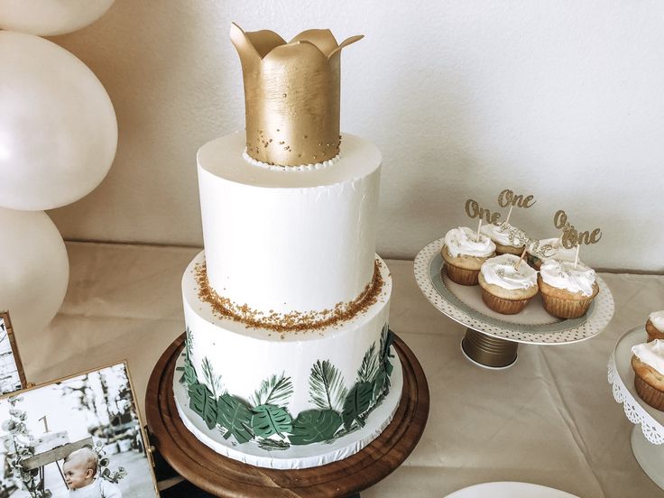 a white and gold wedding cake with cupcakes on the table next to it