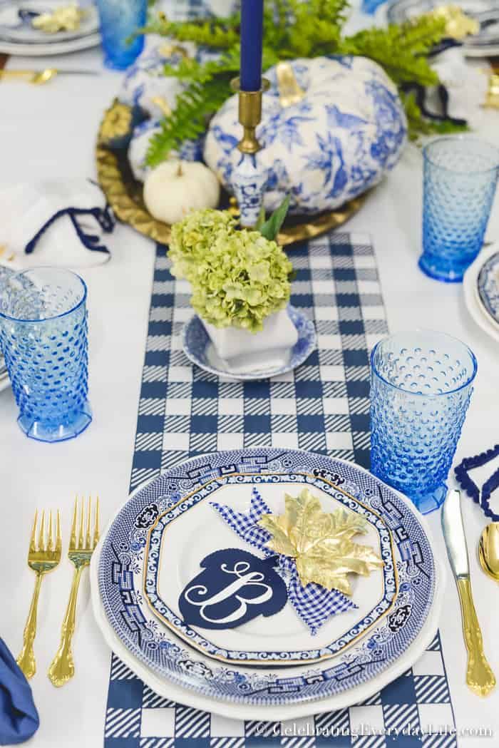 the table is set with blue and white plates, silverware, and gold place settings