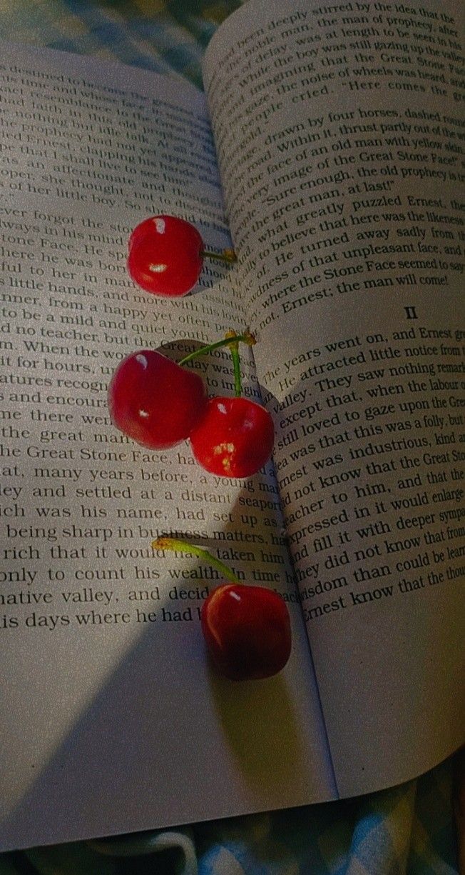 the book is open and has three cherries on it, sitting on a bed