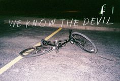 a bike laying on the ground in an empty parking lot that says we know the devil