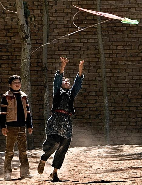 two boys are playing with a kite in front of a brick wall on a sunny day